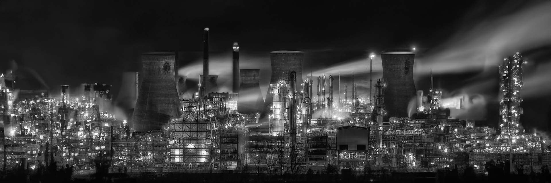 Nighttime view of a large industrial complex with glowing smokestacks, illustrating ENERCA's efforts to modernize traditional energy sectors towards sustainability.