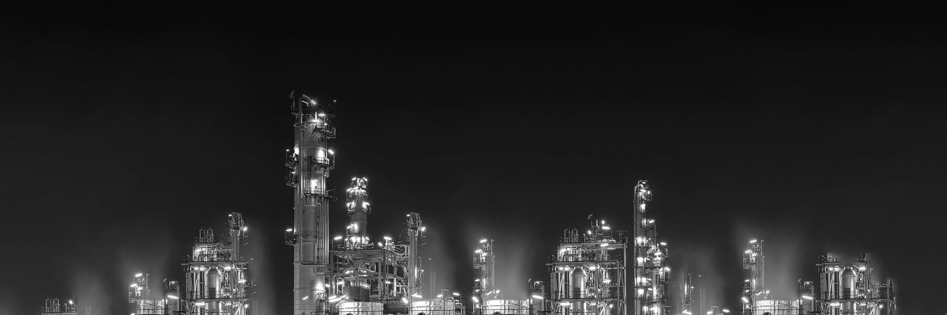 Vast industrial refinery with lit cooling towers emitting smoke at night, symbolizing ENERCA’s mission to drive decarbonization and cleaner energy practices.